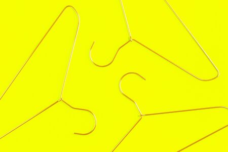 Three pink wire coat hangers on yellow background. Flat lay with copy space for sale or clothes retail or laundry and dry cleaningの写真素材