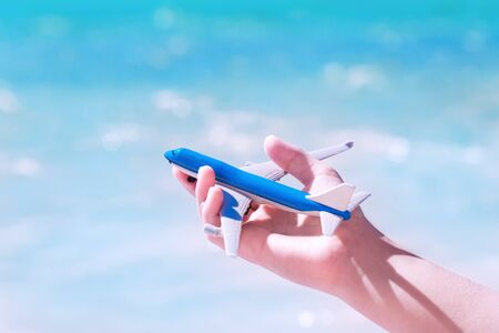 Hand with a toy aircraft against blue turquoise sea ocean waters and sky background. dream travel and exotic vacation concept with copy spaceの写真素材