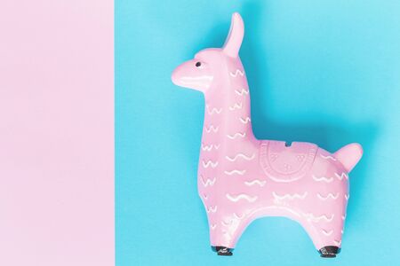 Pink zine type toy alpaca llama on a blue background close up, coin bank. Creative and fun trendy collage of funky animal concept with copy spaceの写真素材