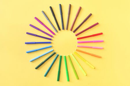Colored rainbow gradient markers arranged as sunshine rays on yellow background. Flat lay with copy...