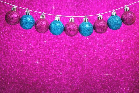 Christmas blue and pink shiny baubles garland with sparks on bright festive pink glitter background. Merry Christmas or Happy new year card concept in rich colors with copy spaceの写真素材