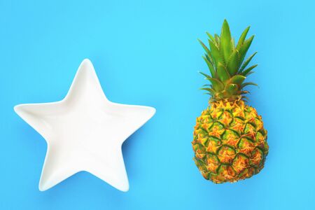 Small pineapple fruit and white star bowl on blue background. Flat lay with copy space. Exotic or healthy eatingの写真素材