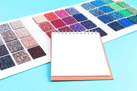 Multicolored carpet swatches catalogue book and notepad on blue desk background. Interior or...