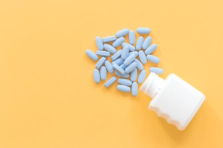 Bblue tablets pills falling out of container on yellow background. Healthcare farmacy and medicine safe consumption concept with copy spaceの写真素材