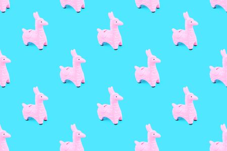 Pink zine type toy alpaca llama on blue background close up, coin money bank. Creative and fun trendy collage of funky animal saving for travel concept banner with copy spaceの写真素材