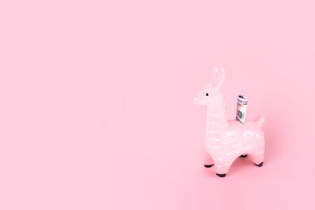 Pink zine type toy alpaca llama with dollar note on monochromatic background close up, coin money bank. Creative and fun trendy collage of funky animal saving for travel concept with copy spaceの写真素材