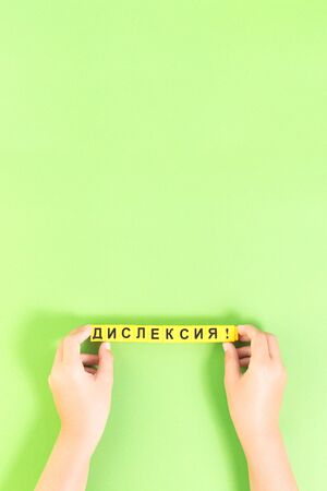 Hands of child with Dyslexia word cubes in Russian language on green background, reading difficulty awareness and disorder concept. Education and neurology with copy spaceの写真素材