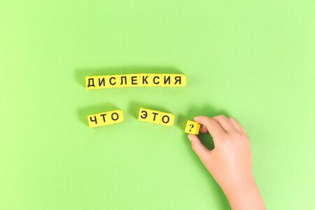 Hands of child with Dyslexia word cubes in Russian language on green background, reading difficulty awareness and disorder concept. Education and neurology with copy spaceの写真素材