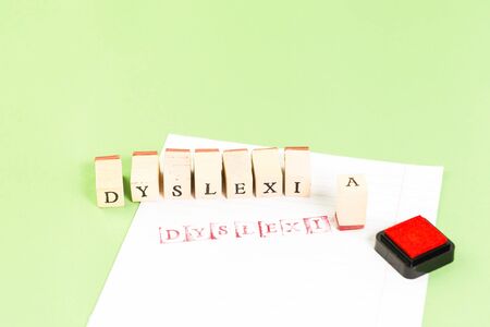 Dyslexia word stamped on ruled paper with red ink on green background, reading difficulty awareness and disorder concept. Education and neurology with copy spaceの写真素材
