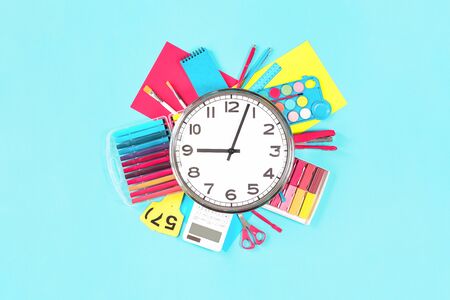 Clock over office or school sets of multicolored bright stationery on pastel blue background. Flat...