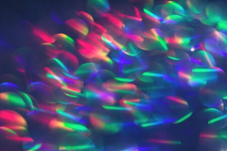 Multicolor blurred neon lights star flares and rainbow glitter on dark background. Bokeh lens flare glow. Festive backdrop with selective focus. Christmas New Year fireworksの写真素材