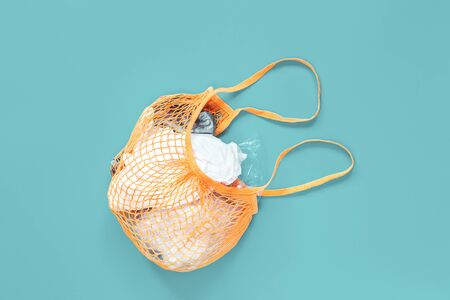 Orange Crochet net bag stuffed with old plastic bags on blue background, creative flat lay for environment friendly zero waste and palstic free ecological life concept. Copy spaceの写真素材