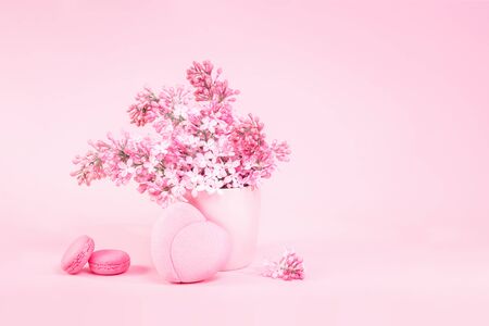 Lilac bouquet in a vase with pink heart jewelry box and space for text on feminine pink background with two macaroons. Love anniversary Mothers Day or valentines card with copy spaceの写真素材