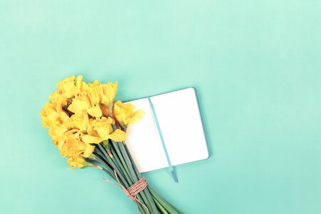 Daffodils bouquet with open notebook on mint green background. Flat lay with copy space, Valentines Womens or Mother Day celebration greeting card or bloggers mock upの写真素材