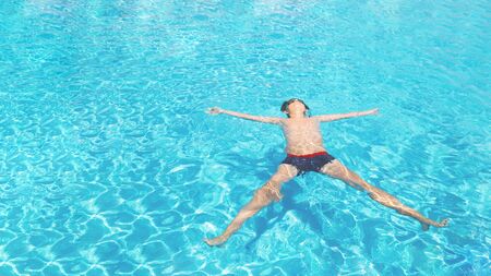 Child caucasian tanned boy swimming or floating as star at the seaside beach or sunny swimming pool....