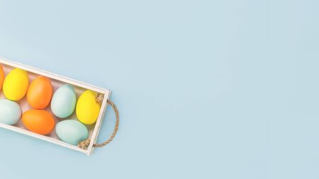 Happy Easter greeting card with yellow, orange and blue pastel dyed easter eggs in a white wooden chest with copy space on blue, flat lay bannerの写真素材