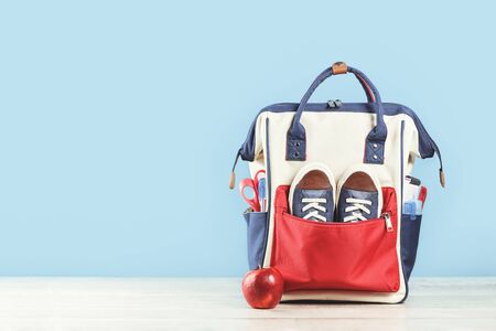 Backpack with school red and blue stationery supplies, notebooks pencils scissors with red apple on...