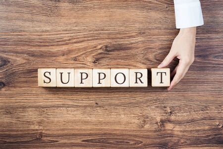 Support text on building blocks on rustic wooden background. Female hand holds the last block. Medical, phsycological technical. Financial or customer support. Business or education with copy spaceの写真素材