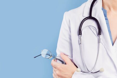 Hand of female doctor ophthalmologist or optician holds pair of glasses with thin metal frame. Minimal banner, blue background. Copy space. Optics oculist, eye test checkups. Medicine mockup templateの写真素材