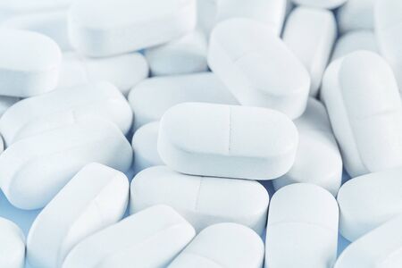 Medical background of many white capsule tablets or pills on the table. Close up. Healthcare farmacy...