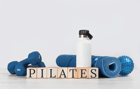 PILATES text. Rolled blue yoga mat and excersise resistance band dumbbells on grey wooden surface. Gender neutral fitness and exercise concept with copy space. Active lifestyle. Workout at home or gymの写真素材