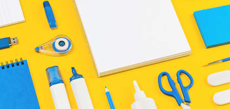 Assorted office and school white and blue stationery on bright yellow background. Organized knolling...