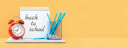 back to school text on Sketchbook and note pad with office supplies and school blue stationery and red alarm clock on desk. education and craft concept. Alarm Clock. Selective focus Copy space. Bannerの写真素材