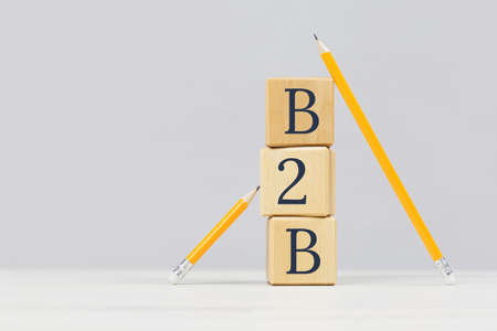 Wooden building blocks with the abbreviation B2B supported by two pencils. Grey background. Business to business marketing solutions ecommerce companies and strategy concept with copy spaceの写真素材