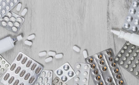 Various pills and tablets and capsules on grey wooden table. Medical border and medication. Health...
