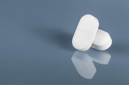 Two white tablets or pills reflected on blue glass. copy space close up view. Medication safe...