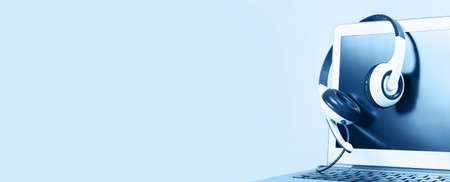 Laptop with blank screen with headphones on white desk blue background and copy space. Distant...