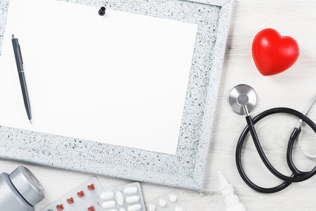 Red heart close up with phonendoscope on grey wooden table. Notice board and various tablets and medication. Health healthcare and medicine. Copy spaceの写真素材
