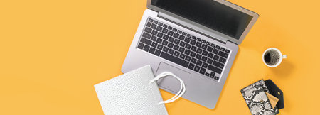 Laptop with gift shopping bags on trendy yellow orange background with coffee cup, credit card in a...