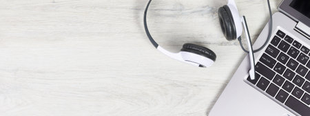 Laptop. keyboard and headphones on grey desk and plain wooden background banner. Helpdesk or call center headset. Distant learning or working from home, online courses or support center concept.の写真素材