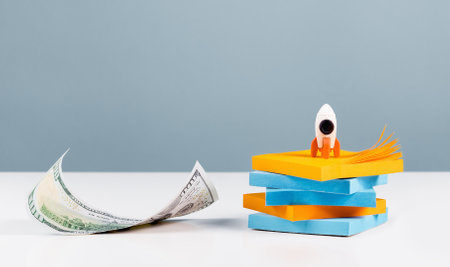 Business or education growth development and success concept banner. Rocket and money stack on white office or home desk with blue background. Innovative thinking. Copy spaceの写真素材