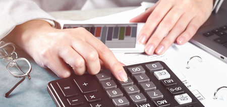 Finance and business concept. Female small business. Hand with calculator on financial graphs on...