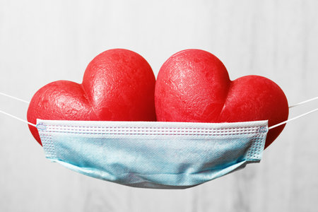 Two red hearts in a face mask hammock. Stay safe at home for holidays. Happy Valentines Day during pandemic. Thank you frontline workers.の写真素材