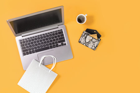 Laptop with gift shopping bags on trendy yellow orange background with coffee cup, credit card in a...