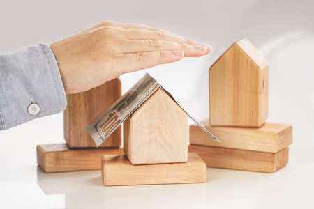 Hands protecting a wooden House with money on roof. real estate mortgage rent sale or insuranceの写真素材