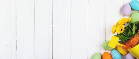 Several bright color dyed easter eggs on wooden background in flat lay with copy space. Border for Happy Easter minimal concept card or banner. Potted spring flowersの写真素材