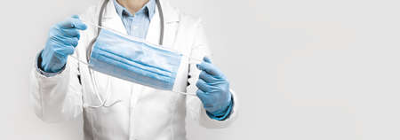 Female Doctor with protective face mask in hands over grey background. Impersonal no face. Medical...
