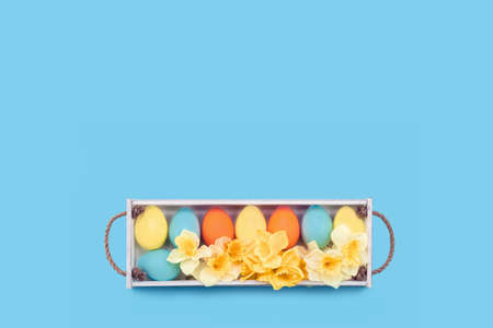 Happy Easter greeting card with yellow, orange and blue pastel dyed easter eggs in a white wooden...