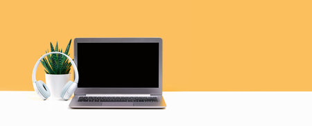 Laptop. Mockup screen and headphones on white desk and plain yellow background banner. Distant learning. working from home, online courses or support minimal concept. call center headsetの写真素材