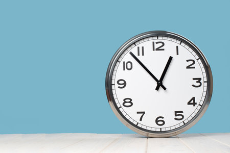 White plain analogue wall clock on trendy pastel blue background. Five past ten oclock. Close up...