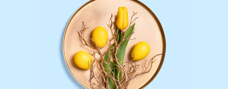 Bouquet of yellow tulips and Easter eggs with golden decor branches on round metal tray. Flat lay on...