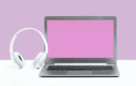 Laptop. Mockup screen and headphones on white desk and plain pink background banner. Distant learning. working from home, online courses or support minimal concept. call center headsetの写真素材