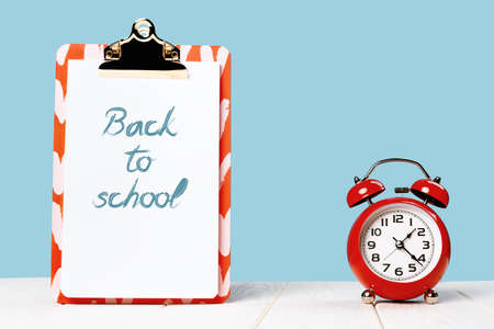 Back to school text notice on note pad and red alarm clock. White wooden desk and blue background. Copy spaceの写真素材