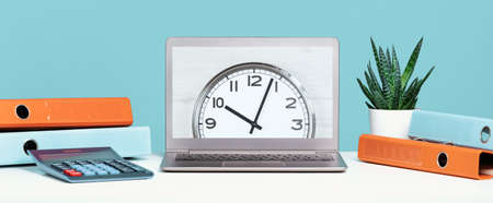 Laptop on office desk with clock in the center and folders, calculator. Ten o'clock. banner with copy space, time management or schedule agenda concept and lunch time. Opening or closing hours.の写真素材