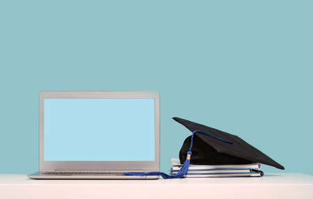 Black Graduation Cap with notebooks on laptop. Masters or Bachelors Degree thesis writing. Knowledge online courses qualifications and higher education with copy space. Lockdown. Mock up screenの写真素材