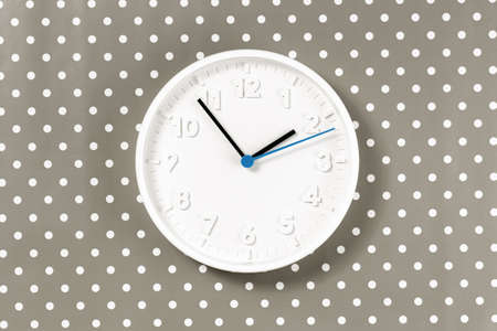 Plain wall clock in the center of polka dot brown gray background. Two o'clock. Close up copy space,...